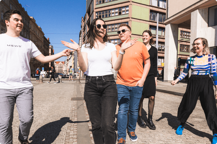Group of five young adults walking and smiling on a city street, engaging in conversation on a sunny day.