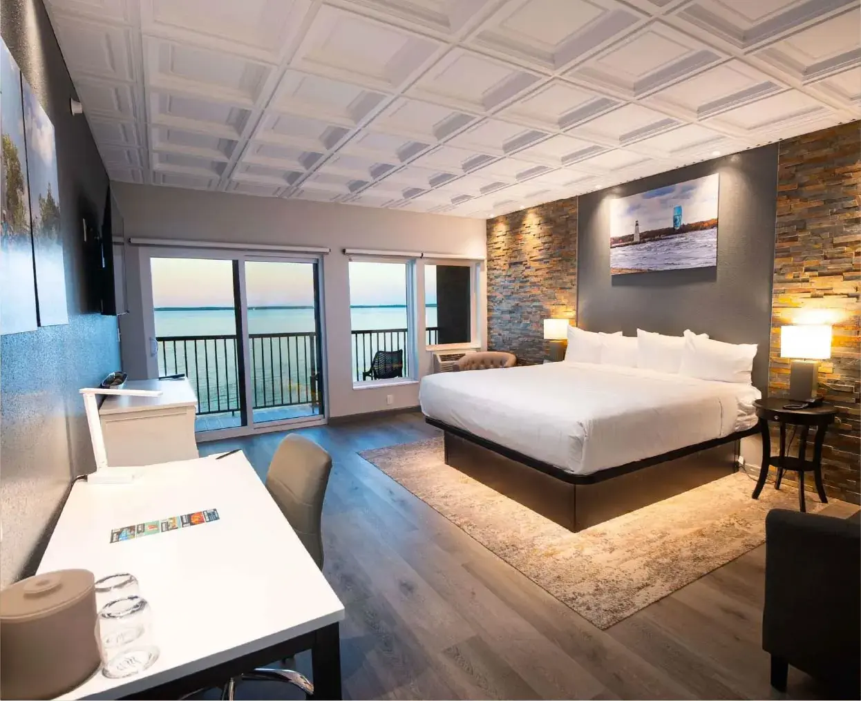 King-sized bed with white bedding against a textured stone accent wall, illuminated by two bedside lamps.
