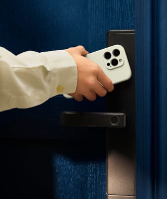 Eine Hand hält ein Smartphone in der Nähe eines digitalen Türschlosses an einer blauen Tür.