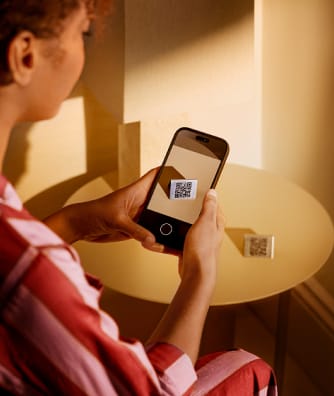 Person scanning a QR code displayed on a smartphone screen with a second QR code on the wall nearby.